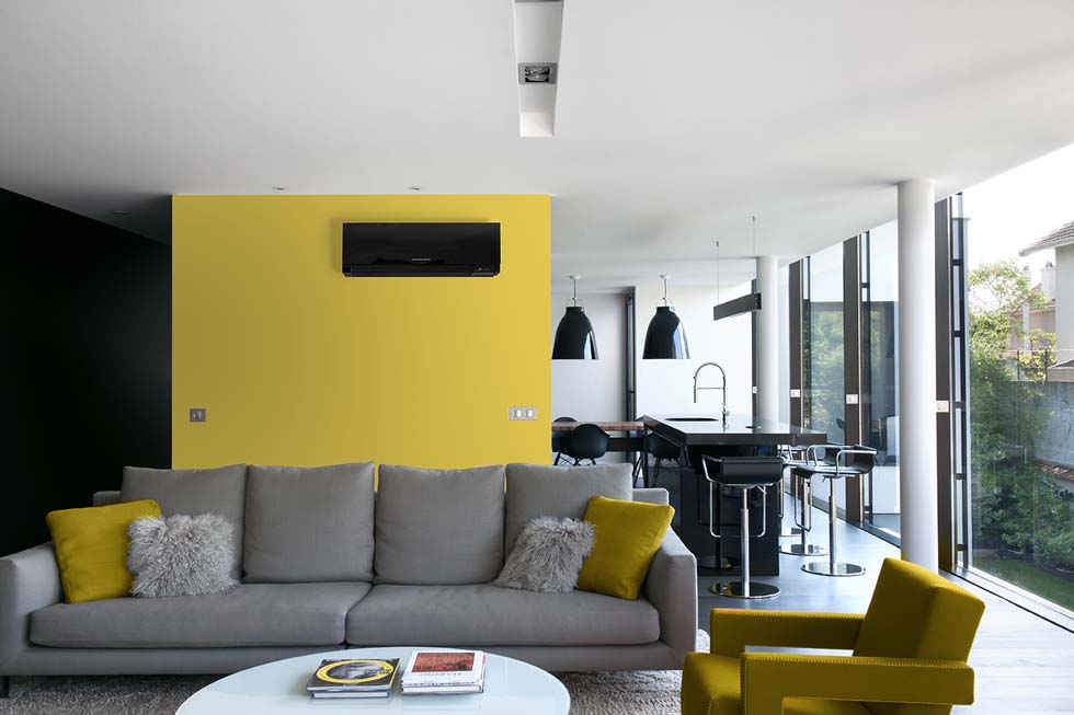 Salon avec canapé, mur jaune et un bloc mutisplit noir en accroché sur le mur